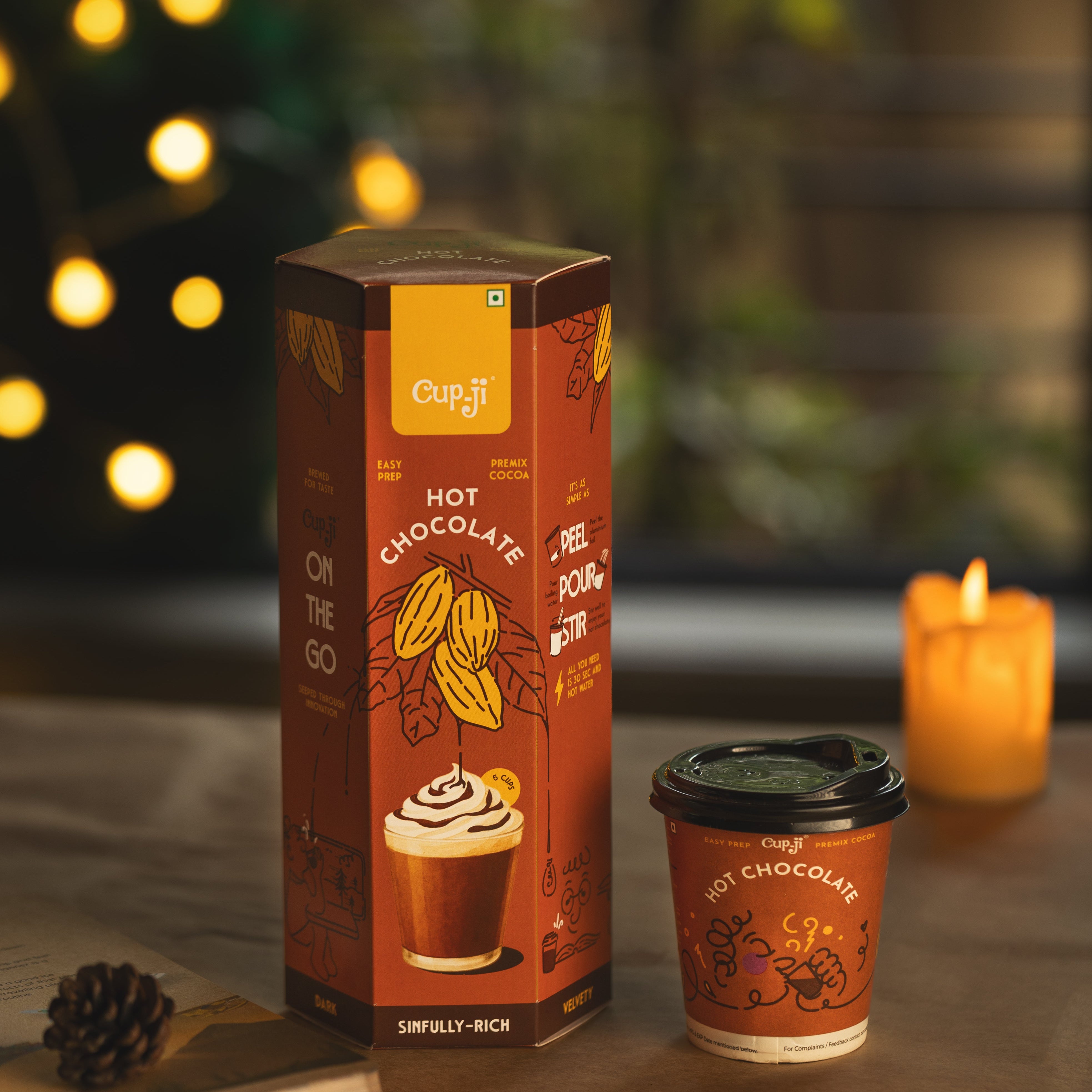 Cupit hot chocolate packaging and cup on a table with a candle in the background