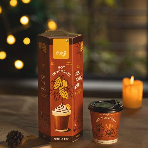 Cupit hot chocolate packaging and cup on a table with a candle in the background